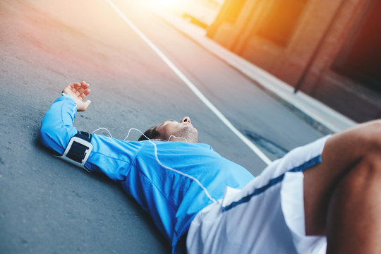 Tired athlete lying on the street after running session and resting at sunset