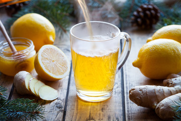 Vitamin black tea with ginger, lemon and honey poured in a cup with steam on a wooden table...