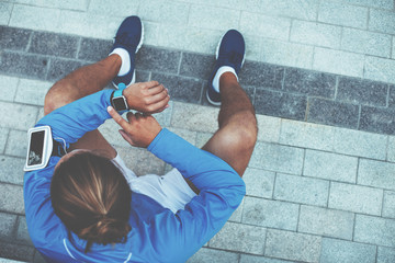 Runner checking results on smart watches, sitting on the street after jogging and resting, armband with mobile phone, earphones with music  © Alex from the Rock