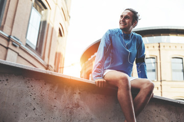 Cheerful male athlete sitting and resting after street workout session