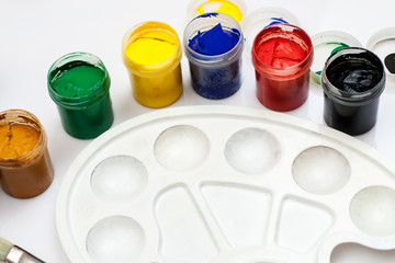 Open gouache jars with empty white plastic palette on a white background