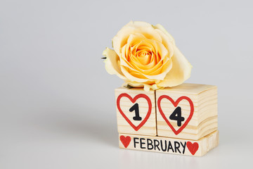 Valentine’s day composition with wooden calendar and yellow rose. Handwritten February, one and four inside red hearts. Bright background. Copy space.