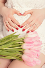 c female hands forming heart shape on belly. pregnant with bouqu