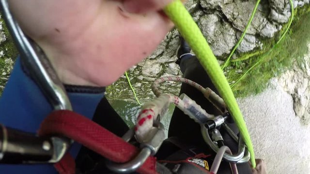 FPV: Man descending steep mossy mountain wall using rope, jumping into the river