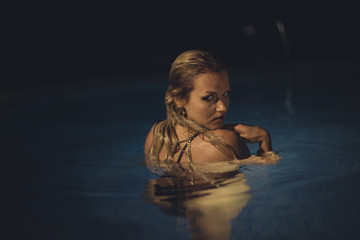 Pretty Blonde in pool at night in summer, summer scene in Spain,