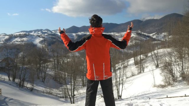 Man making arms raised victory gesture while admiring a winter landscape at the top of the mountains