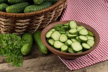 Fresh cucumbers in a brown bowl on the old wooden table.