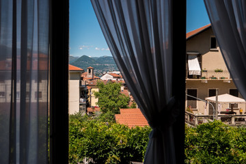 Town and nature behind window. Rooftops and mountains. Picturesque view from hotel room.
