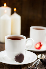 Hot Tea or Chocolate in White Cups with Chocolate Hearts and Lit Candles on Wooden Rustic Background, Valentines Day Concept