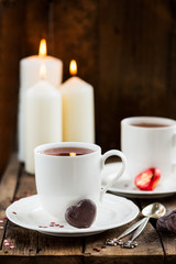 Hot Tea or Chocolate in White Cups with Chocolate Hearts and Lit Candles on Wooden Rustic Background, Valentines Day Concept
