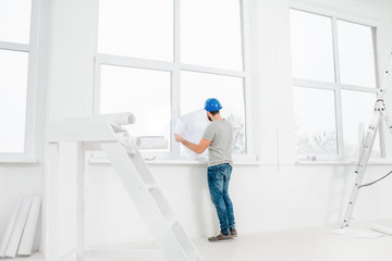 White interior for renovation and repair with ladder, windows and foreman or builder looking at paper drawings