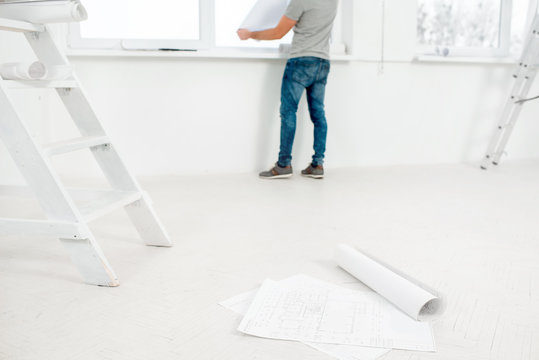 White interior for renovation and repair with ladder, windows and foreman or builder looking at paper drawings