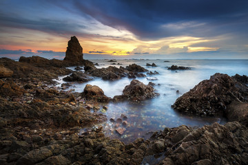Seascape of sea with dramatic wave and rock in sunset.