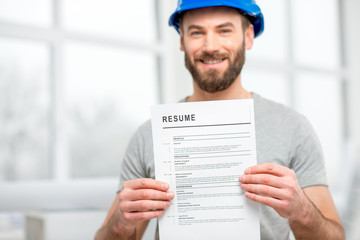 Handsome builder or worker in protective helmet holding his resume standing in the white interior....