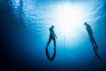 Two free divers, man and woman, ascending from the depth - obrazy, fototapety, plakaty
