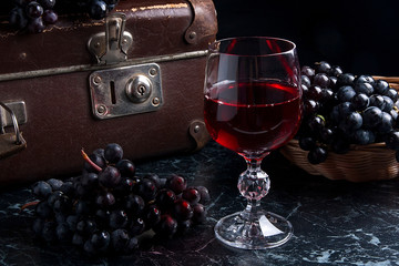 Glass of red wine on dark marble background. Cluster of blue gra