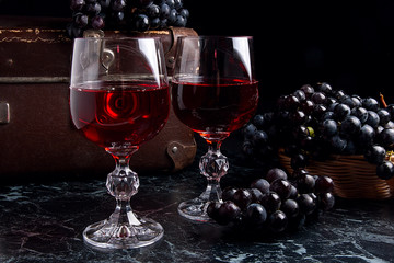 Glass of red wine on dark marble background. Cluster of blue gra