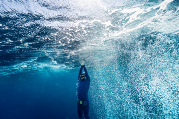 Free diver ascending from the depth in a rough sea with lots of bubbles.