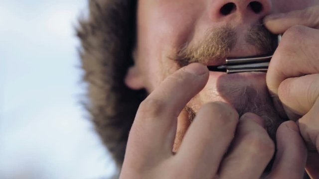 Portrait of a man playing a harp. The bearded shaman plays the harmonica drymba.
