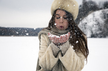Fototapeta premium The girl with dark hair in a bright sheepskin playing in the snow on a background of a winter landscape painting