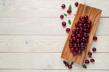 ripe cherries and leaves in a wooden plate on a textured wooden background, view from above