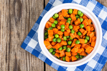 Peas and carrots in a white salad bowl, view from above on a woo