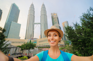 Travel and technology. Young smiling woman taking selfie while walking near Petronas Twins Towers in Kuala-Lumpur, Malaysia, 23 November 2015.