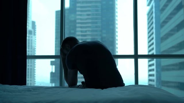 Silhouette of sad, unhappy man admire view sitting on bed at home
