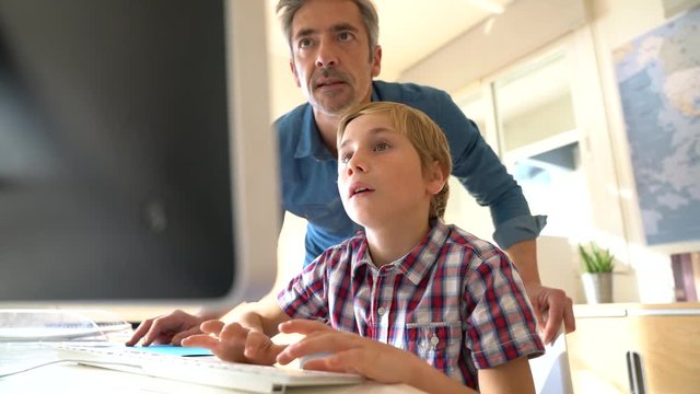 Schoolboy in computer lab with teacher helping