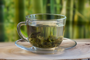 Cup with green tea and green leaves on nature blur background on wooden board.