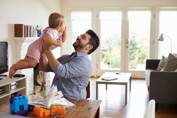 Fototapeta premium Father Sits At Table And Plays With Baby Son At Home