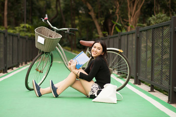 Pretty Thai girl reading book and sitting near by bicycle at the park