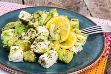 Salad with goat cheese, avocado and olive oil on wood background