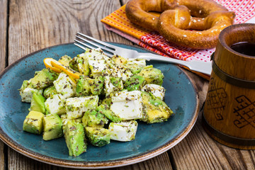 Salad with goat cheese, avocado and olive oil on wood background