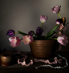 rustic still life. bouquet of tulips in a copper basin on  wooden table. black background