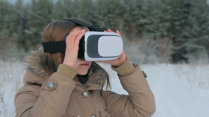 Woman putting on and using virtual reality glasses in winter forest. Virtual reality mask. VR. Future, nature, winter and technology concept