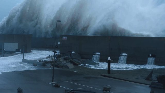 Dramatic slow motion of huge big waves smashing on concrete barrier wall that protects small marina at strong heavy winter storm in sea, early morning or evening low light time