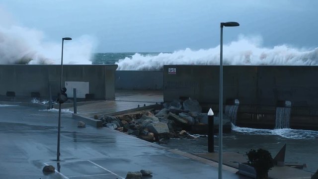 Dramatic slow motion of huge big waves smashing on concrete barrier wall that protects small empty port at strong heavy winter storm in ocean, early morning or evening low light time
