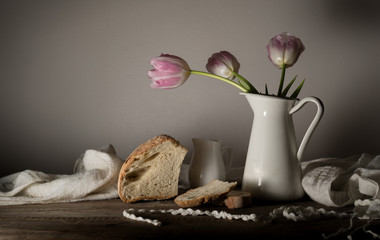 rustic still life. bouquet of tulips, fresh bread, milk on a wooden table. black background