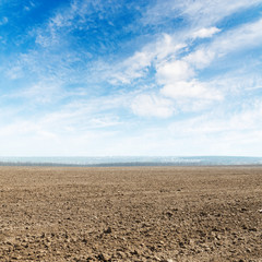 agricultural plowed field and clouds in blue sky over it