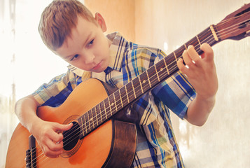Boy learning to play the acoustic guitar. In a blue shirt.