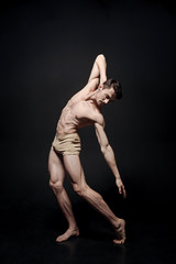 Concentrated young dancer stretching in the black colored studio