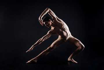 Athletic man doing yoga in the black colored studio
