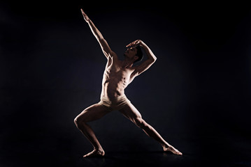 Fototapeta na wymiar Involved young man practicing yoga in the black colored studio