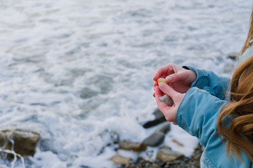 woman's hand holding a wet stone on the shore of the stormy sea