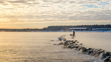 одинокий рыбак на туманном озере с удочкой, ранним утром, зима