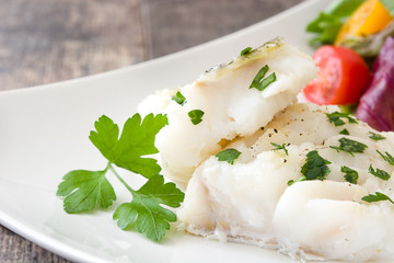 Fried cod fillet and salad on wooden table
