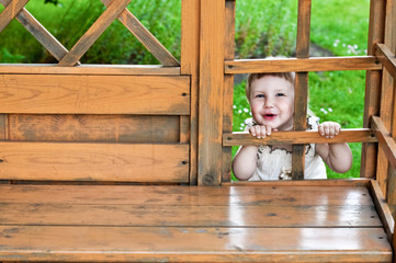 Happy smiling girl looking out between wooden parts of garden house