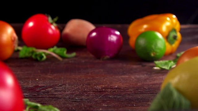 Two onions are moving toward each other on a table. Seasonal vegetables on the table, onion in the foreground. Fresh vegetables: onion, yellow pepper, potatoes, lime tomato on black background. 