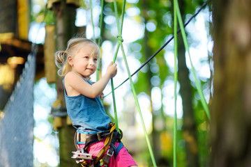 Adorable little girl enjoying her time in climbing adventure park on warm and sunny summer day